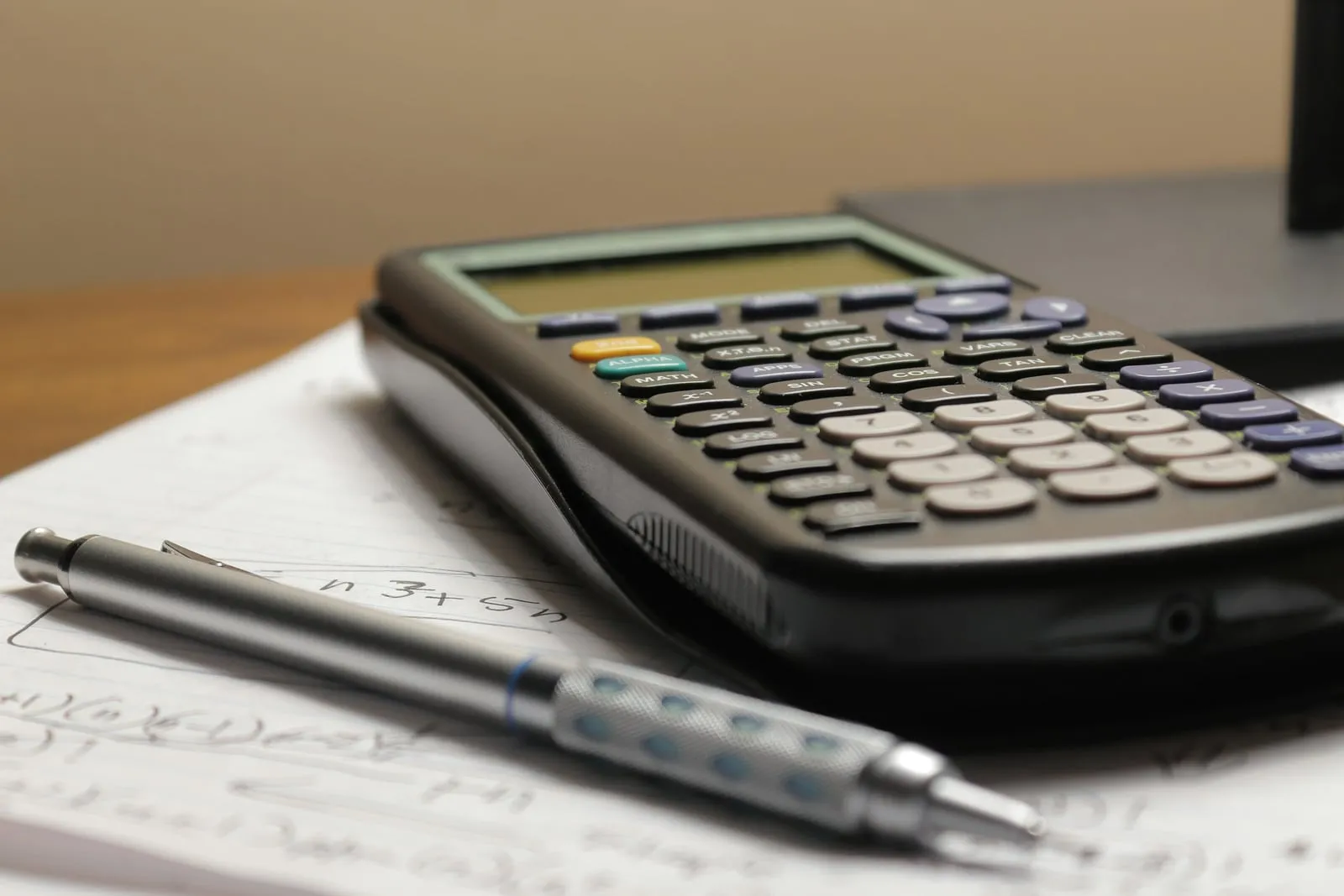 Une calculatrice et un porte-mine posés sur une feuille couverte de calculs, sur un bureau